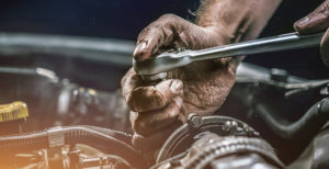 Ölverschmierte Hand mit Schraubwerkzeug in einem Motorraum