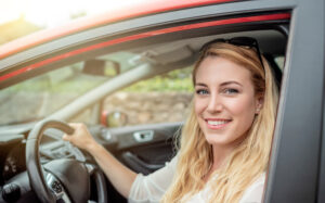Blonde Frau sitzt auf dem Fahrersitz eines Autos und lacht