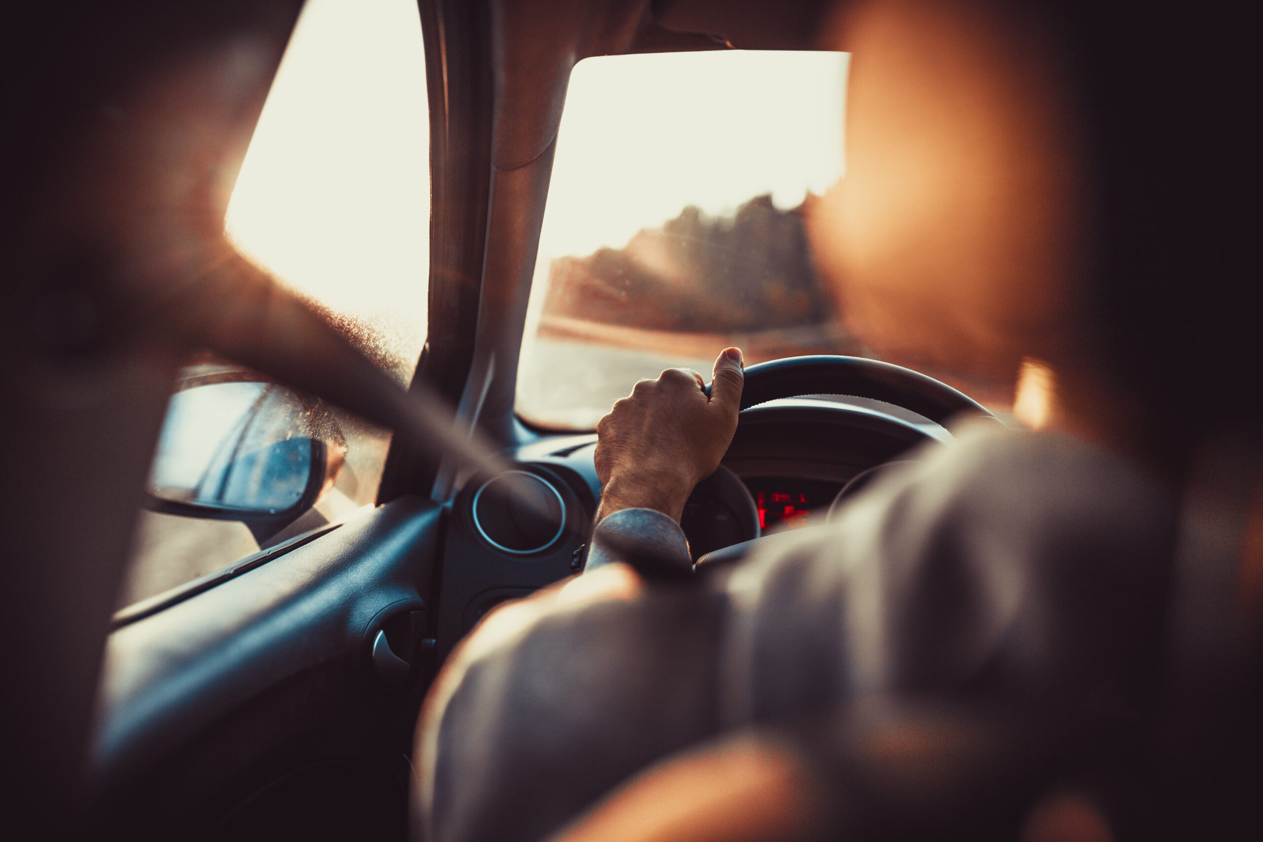 Mann Auto fahren, Hand auf Lenkrad, Blick auf die Straße voraus, Sonnenuntergang.